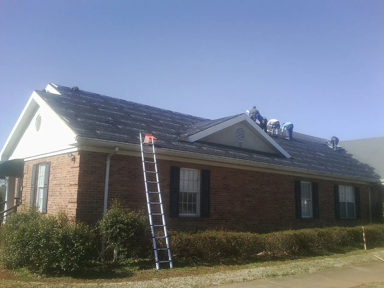 Crew tearing shingles off a brick ranch roof with a ladder set — Metal Roof Repair work by our crew in Ridgewood
