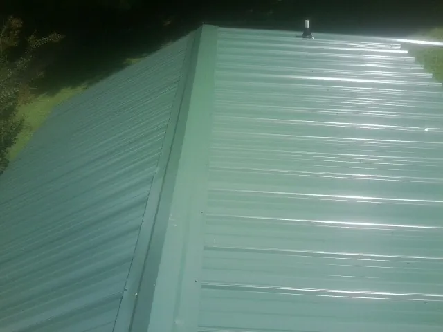 New green metal panels meeting at the ridge of a roof — Flat Roof Repair work by our crew in Ridgewood
