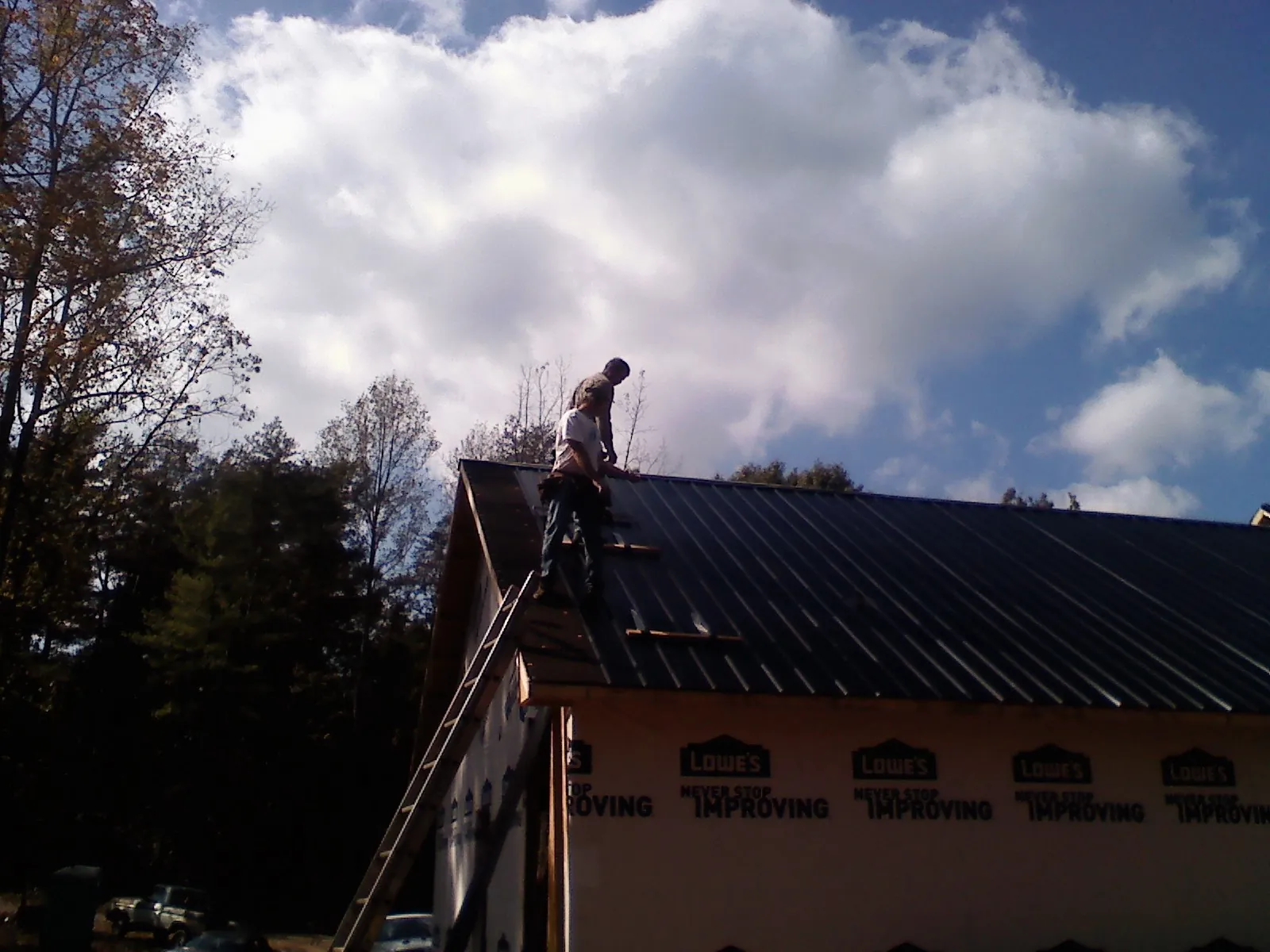 Roofer fastening dark metal panels high against a cloudy sky, from a Roof Inspection job in Ridgewood